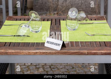 Restaurant reservierte Tischschild mit Weingläsern bereit für eine Party. Eisenschild auf Holztisch mit Wort 'reserviert' auf deutsch Stockfoto