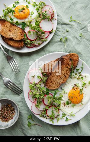 Köstliches Gourmet-Frühstück. Roggenbrot mit Spiegelei, frisch gemahlenem Pfeffer und Salat mit Aufgang und Microgreens. Gesunde Ernährung. Stockfoto