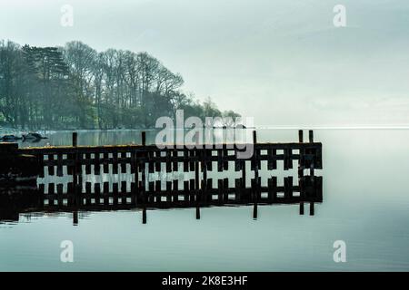An einem ruhigen, ruhigen Frühlingsmorgen spiegelte sich in Ullswater ein ausgedient alter Steg wider. Lake District, Cumbria, England Stockfoto