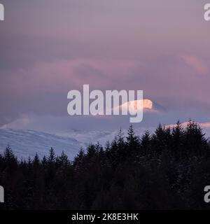 Wunderschöne Alpen Glow treffen Berggipfel in den schottischen Highlands während des atemberaubenden Sonnenaufgangs in der Winterlandschaft Stockfoto