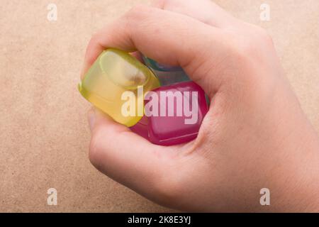 Hand hält gefälschte bunte Eiswürfel auf braunem Hintergrund Stockfoto