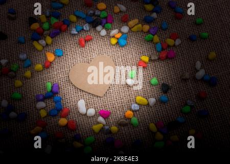 Herz aus Papier inmitten der bunten Steinchen auf Leinwand Boden Stockfoto