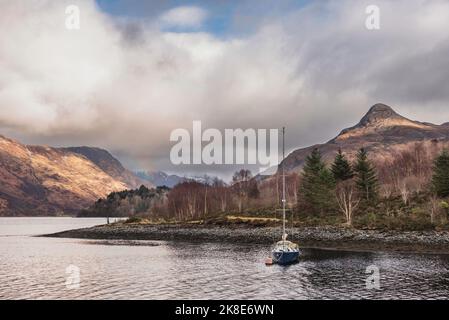 Wunderschöner Blick auf die Winterlandschaft entlang des Loch Leven in Richtung schneebedeckter Berge in der Ferne mit festgedeckter Segelyacht im Vordergrund Stockfoto