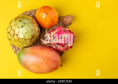 Tropische Herbstfrüchte, Mango, Puderapfel, Pitahaya und Persimmon, auf einem flachen Teller mit einem gelben Hintergrund. Stockfoto