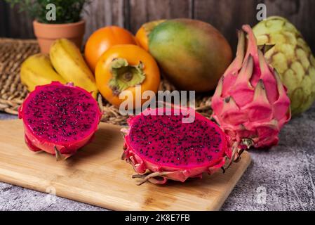 Pitahaya oder Drachenfrucht in zwei Spalten auf einem Holzbrett, die Belichtung der rosa Interieur und schwarze Samen, im Hintergrund einige tropische Früchte wie ch Stockfoto