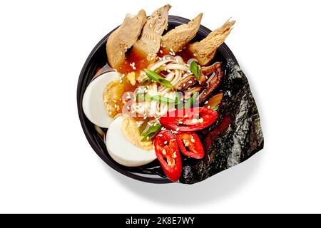 Würzige Ramen-Suppe mit Weizennudeln, Huhn, Shiitake, gekochtem Ei, roten Paprika, grüns, Sesam und Nori Stockfoto