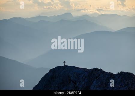 Gipfelkreuz und Bergprofile bei Sonnenuntergang. Österreichische Alpen. Europa. Stockfoto