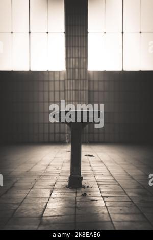 Eine einzige Bank in einem alten Waschraum. Das Licht scheint durch die Fenster. Der ganze Raum ist mit Fliesen gefliest und unter der Decke hängt noch alter Draht Stockfoto