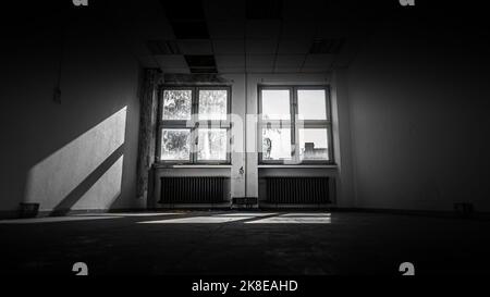 In diesem verlassenen Büro fällt Licht durch zwei alte Holzfenster Stockfoto