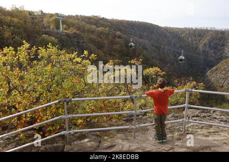 Thale, Deutschland. 23. Oktober 2022. Ein Junge beobachtet die Gondeln der Seilbahn, die über dem Bode-Tal schwebt. Das sonnige Wetter zog wieder viele Besucher in den Harz. Die Betreiber der Bergbahnen und Skilifte im Harz erleben an diesem Wochenende mit Beginn der Herbstferien eine hohe Besucherzahl. Quelle: Matthias Bein/dpa/Alamy Live News Stockfoto