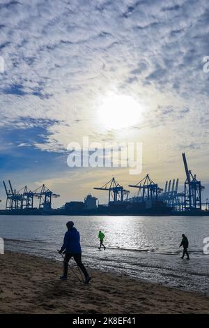 Hamburg, Deutschland. 23. Oktober 2022. Spaziergänger sind am Strand von Övelgönne an der Elbe vor der Silhouette des Hafens. Quelle: Christian Charisius/dpa/Alamy Live News Stockfoto