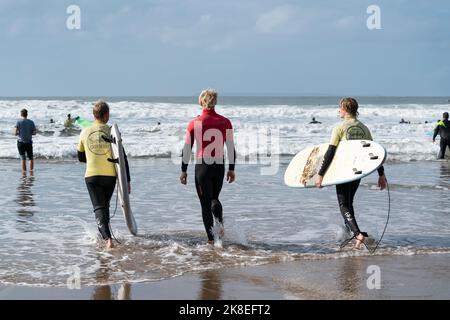 Zwei Surfer begeben sich mit einem Surflehrer (Center) von einer lokalen Surfschule in die Wellen von Croyde Bay, North Devon, Großbritannien. Stockfoto