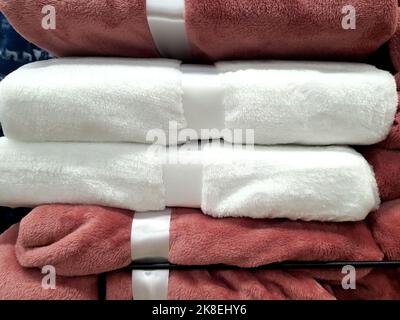 Stapel von warmen Decken, Bettdecken, liegt auf dem Regal. Haushaltsartikel, weich, flauschig im Supermarkt, rosa und weiß Stockfoto