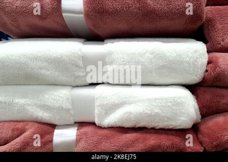 Stapel von warmen Decken, Bettdecken, liegt auf dem Regal. Haushaltsartikel, weich, flauschig im Supermarkt, rosa und weiß Stockfoto