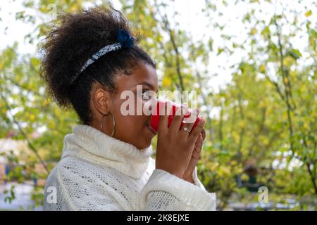 Eine junge afroamerikanische Frau hält im Herbst eine Tasse heißen Tee in der Hand Stockfoto