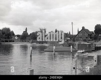 1962, historisch, ein kleines Ausflugsboot, das aus der Bray-Schleuse auf der Themse kommt. Die 1845 erbaute, grassseitige Schleuse befindet sich offiziell auf der Buckinghamshire-Seite der themse, obwohl Bray selbst in Berkshire liegt. Auf dem Bild gesehen, die Hütte des Schleusenwärters, die sich zwischen der Schleuse und dem Wehr befindet. Stockfoto