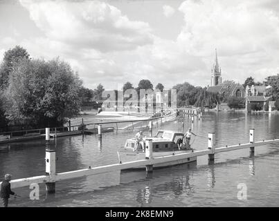 1966, historisch, Blick aus dieser Ära eines Vergnügungsbootes, das auf der Themse in Marlow, Bekshire, England, Großbritannien, festgemacht wurde. In der Ferne sieht man auf dem Bild die Hängebrücke über das Wehr und den Turm der All-Saint-Kirche. Stockfoto