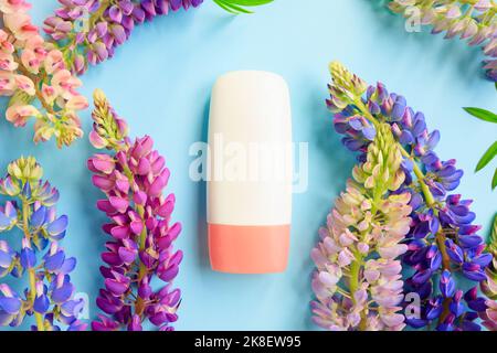 Mockup weiße Kosmetikröhrchen-Flasche mit rosa Schraubverschluss und bunten Lupinen-Blüten viel auf blauem Hintergrund. Feuchtigkeitsspendende Creme, Gel, Hautpflege, Sonne Stockfoto