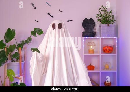 Der Halloween-Geist verwendet ein Mobiltelefon, um im Internet zu surfen, Online-Shops und Märkte zu durchsuchen. Der Geist macht an Halloween eine Bestellung von einem Smartphone. Neonlicht. Stockfoto