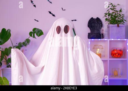 Der Halloween-Geist verwendet ein Mobiltelefon für Anrufe, Glückwünsche, Einschüchterung. Der Geist macht an Halloween eine Bestellung von einem Smartphone. Witziges Halloween-Konzept. Neonlicht. Stockfoto