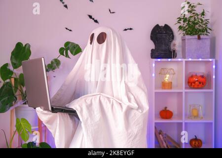 Der Geist von Halloween verwendet einen Laptop, um im Internet zu surfen, um Online-Shops, Märkte zu durchsuchen. Ein Geist macht einen Bestellcomputer für Halloween. Der Geist zahlt für einen Online-Kauf. Neonlicht. Stockfoto