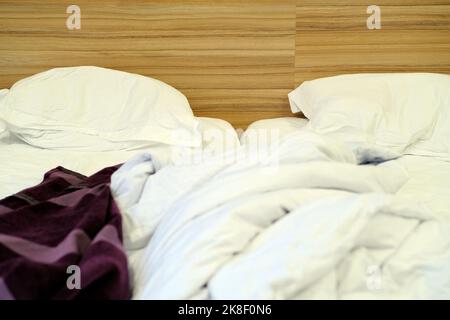 Das Bett war mit Kissen und einer gekrümmten Decke ausgestattet. Zerbröckelte Decke und Kissen auf leerem, zerknittertem Bett im Hotelzimmer nach dem Schlafen in der Nacht. Stockfoto