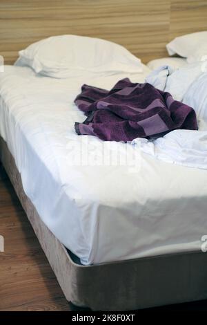 Das Bett war mit Kissen und einer gekrümmten Decke ausgestattet. Zerbröckelte Decke und Kissen auf leerem, zerknittertem Bett im Hotelzimmer nach dem Schlafen in der Nacht. Stockfoto