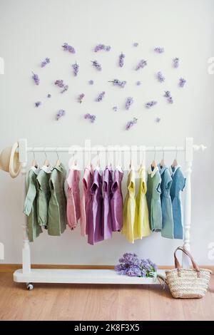 Mehrfarbige Kleider, die auf dem Regal vor der Wand mit Blumen hängen Stockfoto