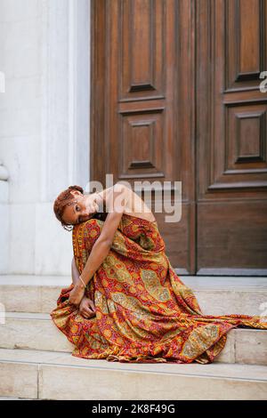 Junge Frau, die Knie umarmt und vor der Tür auf Stufen sitzt Stockfoto