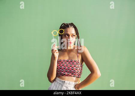 Junge Frau mit Brillenstütze vor der grünen Wand Stockfoto