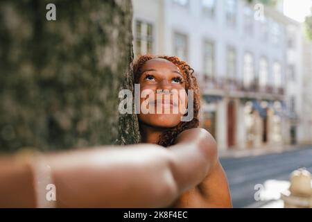 Lächelnde junge Frau umarmt Baumstamm Stockfoto