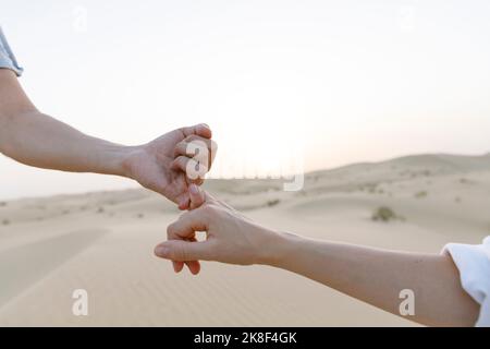 Hände eines Paares, das bei Sonnenuntergang kleine Finger in der Wüste hält Stockfoto