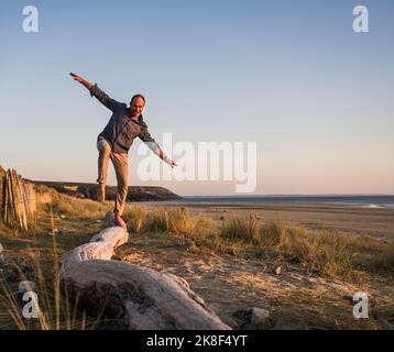 Verspielter Mann mit ausgestreckten Armen, der auf dem Holzstamm balanciert Stockfoto