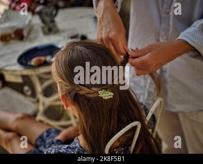 Mutter flechtet die Haare der Tochter mit Blumen auf dem Dach Stockfoto