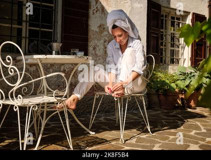 Reife Frau mit einem Handtuch, das Nagellack auf die Zehennägel auf dem Dach aufgibt Stockfoto