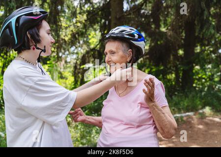 Mädchen helfen Urgroßmutter trägt Fahrradhelm im Park Stockfoto