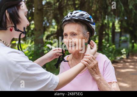 Urenkelin hilft älteren Frauen mit Fahrradhelm im Park Stockfoto