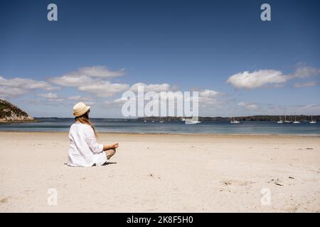 Reife Frau praktiziert Meditation am Strand Stockfoto