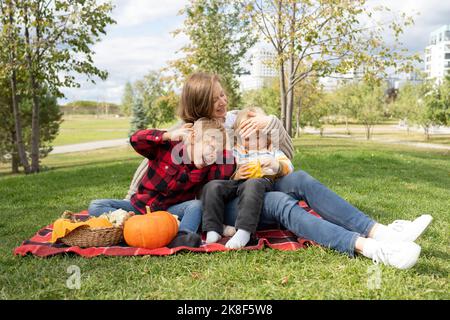 Fröhliche Jungen mit Mutter, die im Park auf einer Picknickdecke sitzt Stockfoto