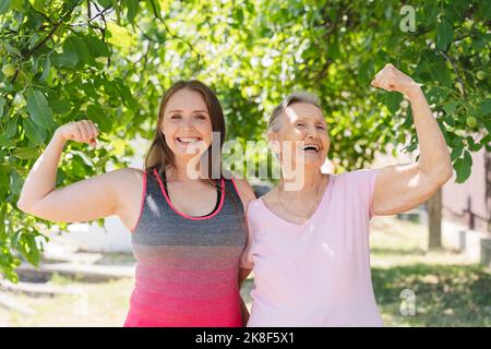 Aktive ältere Frau, die Muskeln anbiegend, mit einem Fitnesstrainer im Park Stockfoto