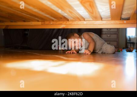 Glücklicher Junge, der zu Hause unter dem Bett schaute Stockfoto