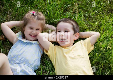 Fröhlicher Junge mit Schwester, der sich im Park auf Gras entspannt Stockfoto