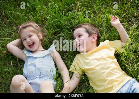 Fröhliche, niedliche Geschwister, die sich im Park auf dem Rasen entspannen Stockfoto