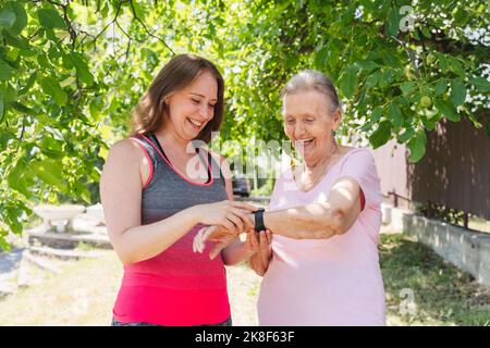 Fröhlicher Fitnesstrainer, der älteren Frau im Park eine intelligente Uhr beibringt Stockfoto