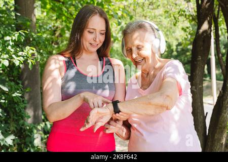 Lächelnder Fitnesstrainer, der älteren Frau im Park eine intelligente Uhr beibringt Stockfoto