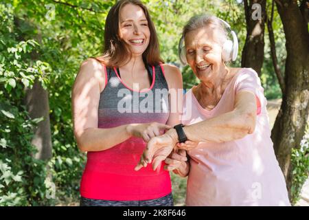 Fröhlicher Fitnesstrainer mit einer älteren Frau, die im Park eine intelligente Uhr trägt Stockfoto