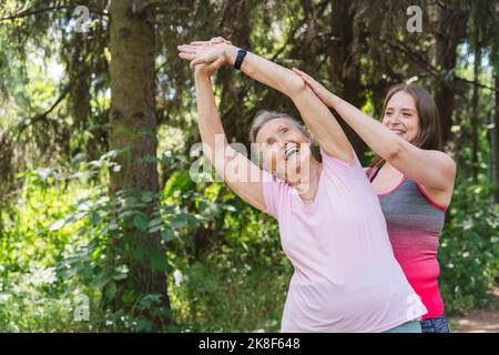 Ein glücklicher Fitnesstrainer, der die ältere Frau beim Training vor dem Baum im Park begleitet Stockfoto