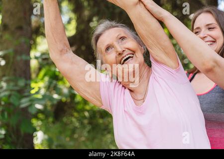 Ein glücklicher Fitnesstrainer, der die ältere Frau beim Training im Park begleitet Stockfoto