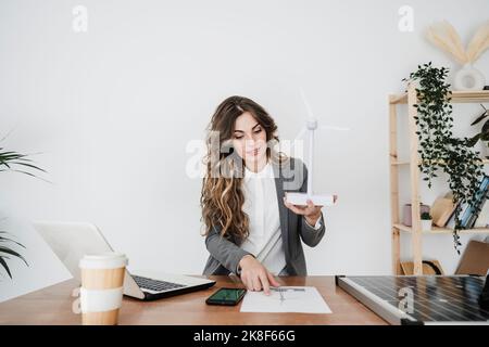 Junge Ingenieurin, die in einem modernen Büro mit Windturbinenmodell arbeitet Stockfoto