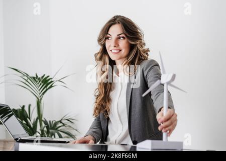 Junge Geschäftsfrau mit Windturbinenmodell im modernen Büro Stockfoto